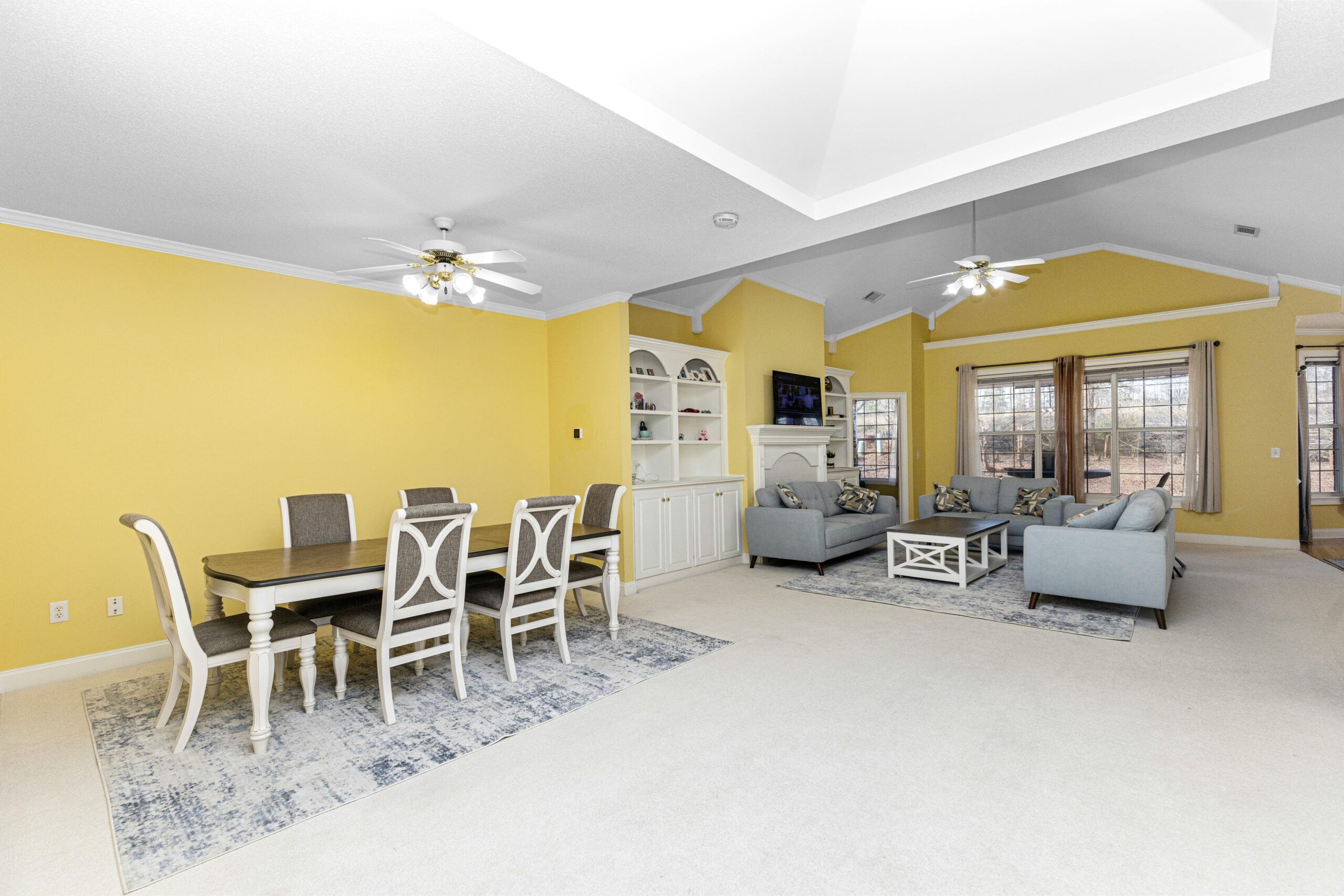 Open-concept living and dining room with yellow walls, elegant furnishings, natural light.