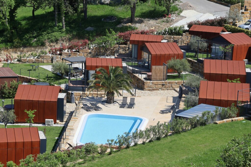 Aerial view of a modern resort featuring red roof cabins and a central swimming pool.